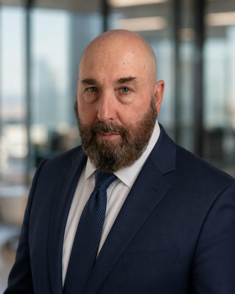 Dr. Neal McLoughlin in a navy suit and blue tie in an office