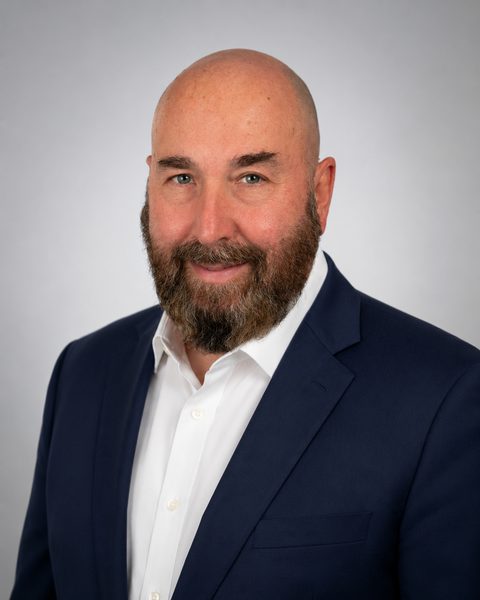 Dr. Neal McLoughlin smiling, wearing a navy suit and white shirt